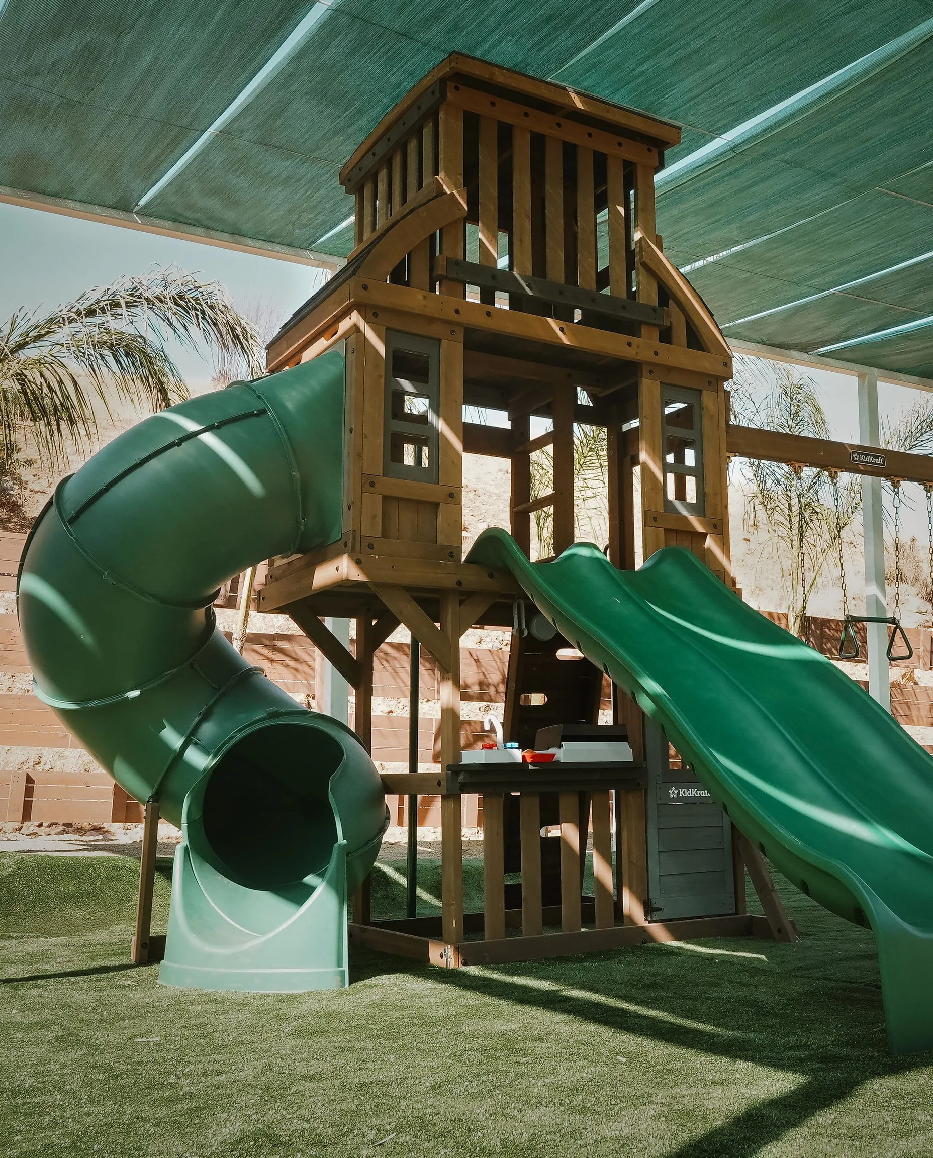 The wooden play structure and its slides, under its shade sail