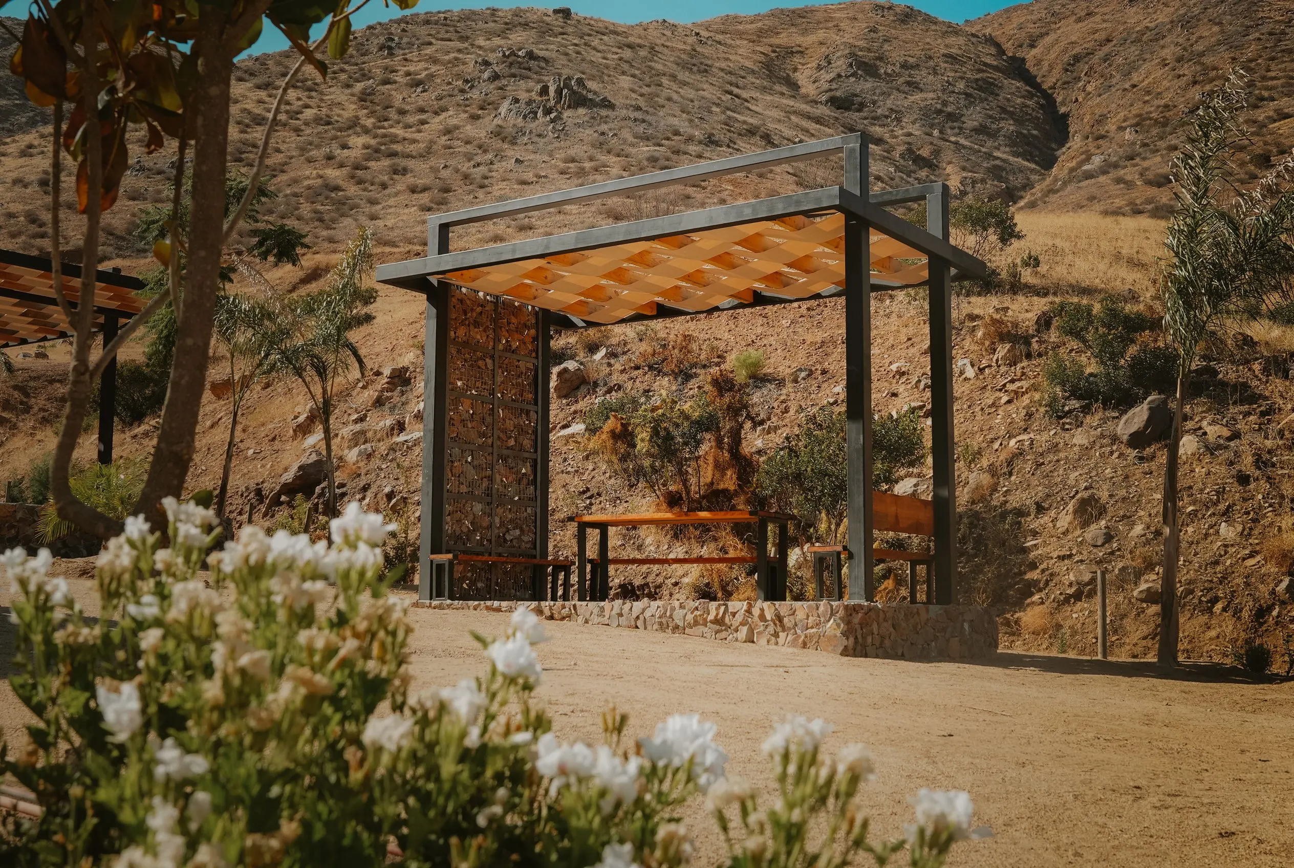 A wooden palapa with an orange shade sail, among the hills